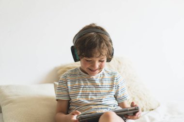 Evdeki yatakta uzanıp bilgisayar tabletleriyle oynayan, internetten kitap okuyan ve kablosuz kulaklıkla müzik dinleyen tatlı çocuk.