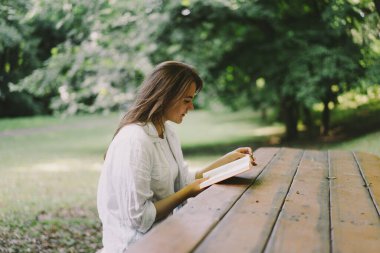 Woman holds book in her hands. Reading the book sitting on a bench at outdoors
