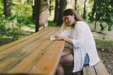 Woman holds book in her hands. Reading the book sitting on a bench at outdoors
