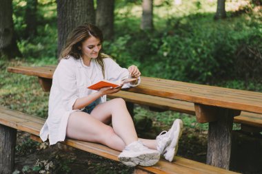 Woman holds book in her hands. Reading the book sitting on a bench at outdoors