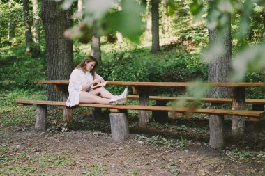 Woman holds book in her hands. Reading the book sitting on a bench at outdoors