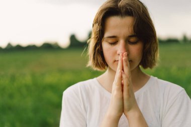 Teenager Girl closed her eyes, praying. Hands folded in prayer concept for faith, spirituality and religion. Peace, hope, dreams concept