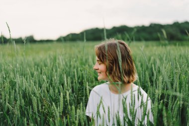 Beautiful teen girl in a field of green wheat. Field of green wheat. Happy Cheerful Teen Girl walking in nature.