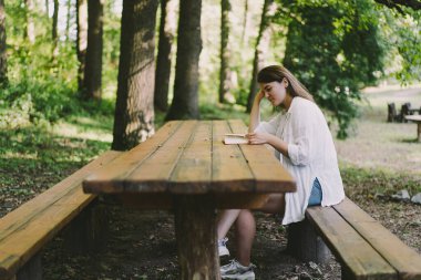 Woman holds book in her hands. Reading the book sitting on a bench at outdoors