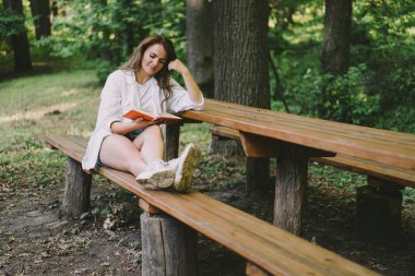 Woman holds book in her hands. Reading the book sitting on a bench at outdoors