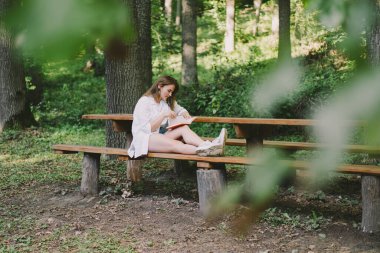 Woman holds book in her hands. Reading the book sitting on a bench at outdoors