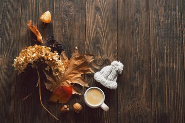 Autumn composition. Cup of coffee and autumn dried leaves, knitted little hat on wood background. Flat lay, top view