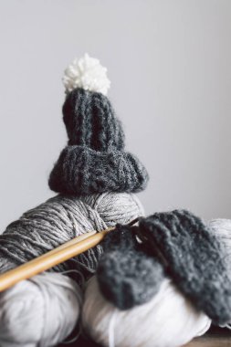Balls of wool yarn, knitted little hat and wooden knitting needles on wooden background. Hobby craft. Concept of knitting, needlework.