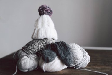 Balls of wool yarn, knitted little hat and wooden knitting needles on wooden background. Hobby craft. Concept of knitting, needlework.