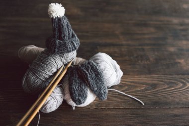 Balls of wool yarn, knitted little hat and wooden knitting needles on wooden background. Hobby craft. Concept of knitting, needlework.