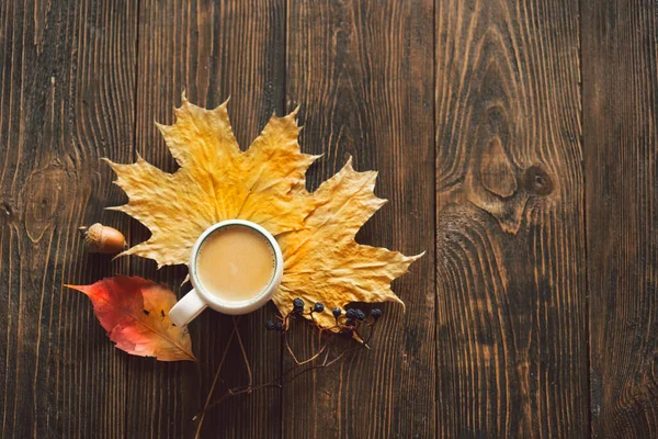 Autumn composition. Cup of coffee and autumn dried leaves on wood background. Flat lay, top view