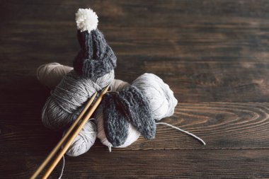 Balls of wool yarn, knitted little hat and wooden knitting needles on wooden background. Hobby craft. Concept of knitting, needlework.