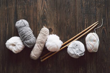 Balls of wool yarn, knitted little hat and wooden knitting needles on wooden background. Hobby craft. Concept of knitting, needlework.