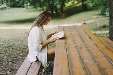 Woman holds book in her hands. Reading the book sitting on a bench at outdoors