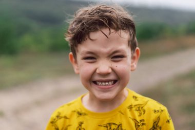 A six year old boy smiles at the camera in the park. Happy child boy laughing and playing in the summer day