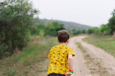 A six-year-old boy is standing with his back in the countryside. Back view. Happy child boy laughing and playing in the summer day.