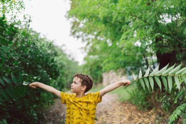 A six-year-old boy runs with green leaves in his hands in the countryside. Happy child boy laughing and playing in the summer day.