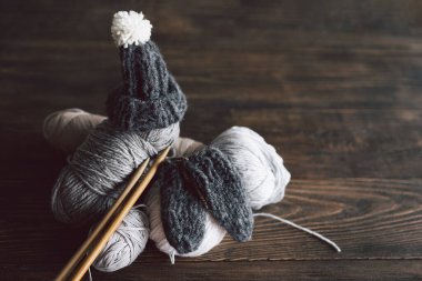 Balls of wool yarn, knitted little hat and wooden knitting needles on wooden background. Hobby craft. Concept of knitting, needlework.