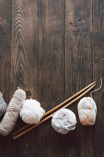 Balls of wool yarn, knitted little hat and wooden knitting needles on wooden background. Hobby craft. Concept of knitting, needlework.
