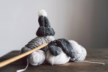 Balls of wool yarn, knitted little hat and wooden knitting needles on wooden background. Hobby craft. Concept of knitting, needlework.