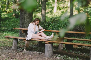 Woman holds book in her hands. Reading the book sitting on a bench at outdoors