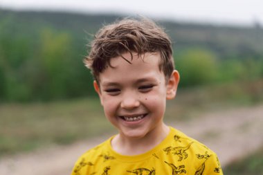 A six year old boy smiles at the camera in the park. Happy child boy laughing and playing in the summer day