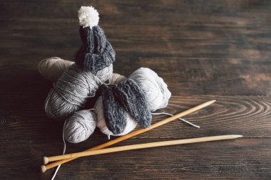 Balls of wool yarn, knitted little hat and wooden knitting needles on wooden background. Hobby craft. Concept of knitting, needlework.