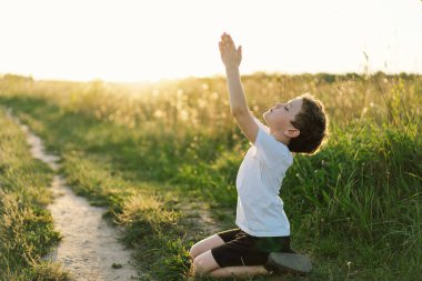 Oğlan gözlerini kapattı ve gün batımında bir tarlada dua etti. İnanç, maneviyat ve din için dua kavramına sarılmış eller..