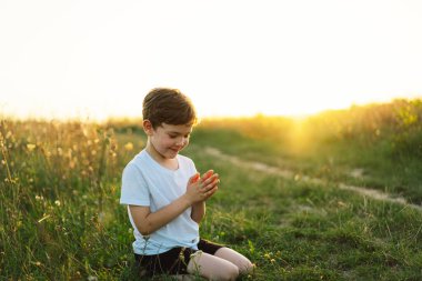 Oğlan gözlerini kapattı ve gün batımında bir tarlada dua etti. İnanç, maneviyat ve din için dua kavramına sarılmış eller..