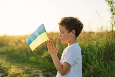 Ukraynalı çocuk gözlerini kapadı ve Ukrayna 'daki savaşı gün batımında bir tarlada durdurmak için dua etti. İnanç, maneviyat ve din için dua kavramında eller kavuşturuldu. Rusya 'nın Ukrayna' ya karşı savaşı. Savaşı Durdur