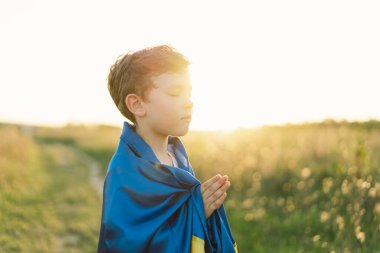 Ukraynalı çocuk gözlerini kapadı ve Ukrayna 'daki savaşı gün batımında bir tarlada durdurmak için dua etti. İnanç, maneviyat ve din için dua kavramında eller kavuşturuldu. Rusya 'nın Ukrayna' ya karşı savaşı. Savaşı Durdur