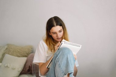 Genç bir kız yatak odasında resim yapıyor ya da ödev yapıyor. Evde okuyan bir genç. Okula geri dön.