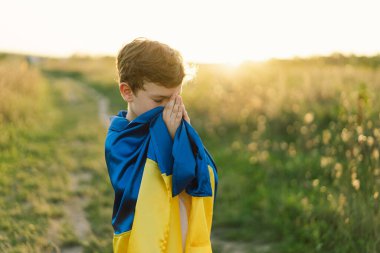 Ukraynalı çocuk gözlerini kapadı ve Ukrayna 'daki savaşı gün batımında bir tarlada durdurmak için dua etti. İnanç, maneviyat ve din için dua kavramında eller kavuşturuldu. Rusya 'nın Ukrayna' ya karşı savaşı. Savaşı Durdur