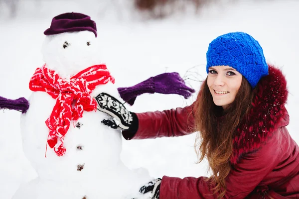 Hübsches Mädchen mit Schneemann im Kiefernwald an einem Wintertag — Stockfoto