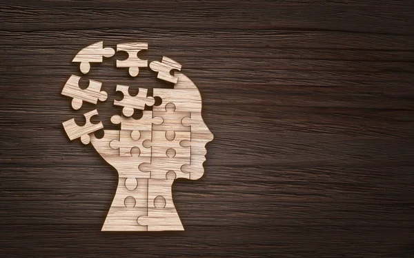 Symbol duševního zdraví. Lidská hlava silueta s puzzle vystřižené z dřevěného pozadí — Stock fotografie