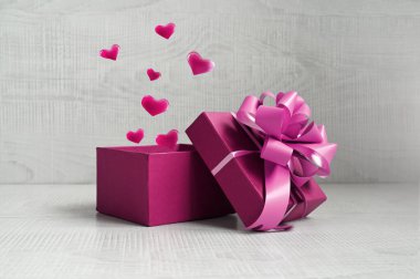 Gri arka planda kalplerden gelen havai fişeklerle dolu tek bir kırmızı hediye kutusu. Tatil kavramı.