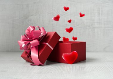 Gri arka planda kalplerden gelen havai fişeklerle dolu tek bir kırmızı hediye kutusu. Tatil kavramı.