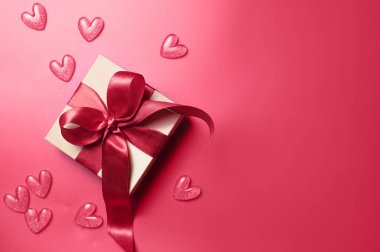 Sevgililer Günü süslemelerinin en üst görüntüsü kırmızı kurdeleli beyaz hediye kutusu ve izole edilmiş kırmızı arka planlı küçük kalpler boş alan.