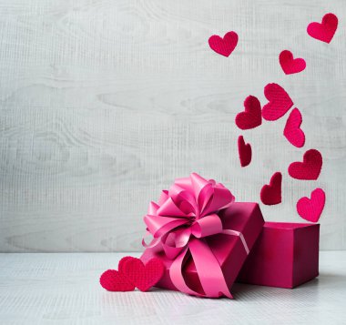 Gri arka planda kalplerden gelen havai fişeklerle dolu tek bir kırmızı hediye kutusu. Tatil kavramı.