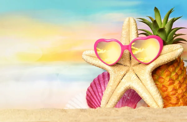 Sıcak kumsalda ananas, denizyıldızı ve güneş gözlüğü olan tropikal bir deniz. Kopya alanı ile seyahat ve tatil kavramı.