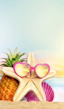 Sıcak kumsalda ananas, denizyıldızı ve güneş gözlüğü olan tropikal bir deniz. Kopya alanı ile seyahat ve tatil kavramı.