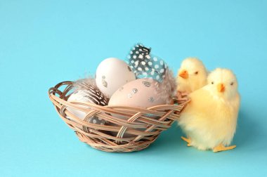 Mavi arka planda tüyleri ve yavruları olan bir yuvada paskalya yumurtaları. Tatil kavramı.