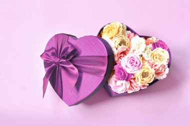 Kalp şeklinde hediye kutusu ve buket. Çiçekler kalp şeklinde bir hediyedir. Pembe arka planda bir kutunun içindeki güller.
