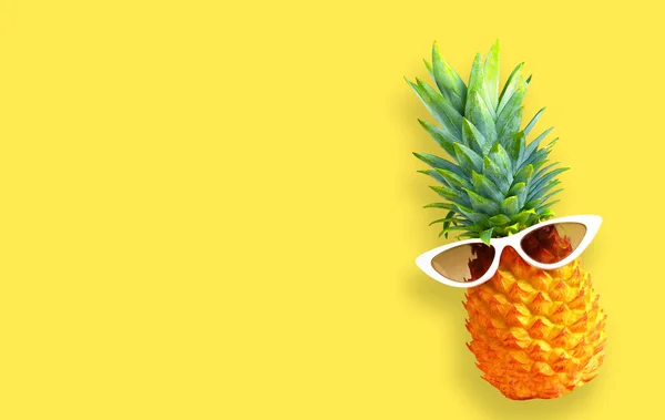 Summer background. Funny pineapple in sunglasses on yellow background.