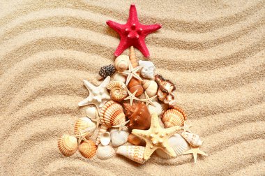 Christmas tree with different seashells on the sea sand. Creative Christmas background