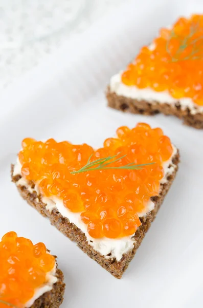 Sanduíche com caviar vermelho na forma de um coração na placa branca — Fotografia de Stock