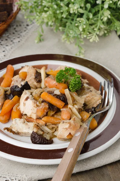 Stufato di pollo con carote e prugne su un piatto, primo piano — Foto Stock