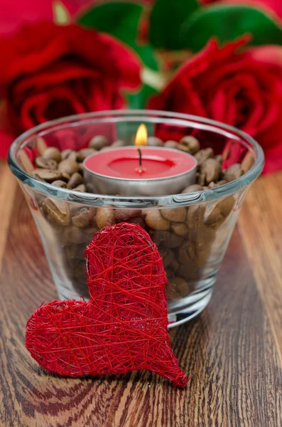 Vela roja en una taza de vidrio con granos de café y corazón decorativo — Foto de Stock