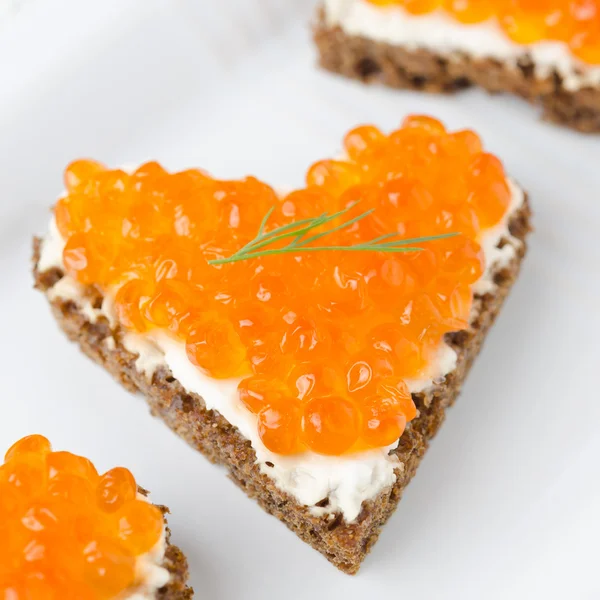 Smörgås med röd kaviar i form av ett hjärta på vit platta — Stockfoto