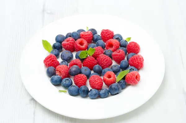 Fresh raspberries and blueberries on a white plate — Stok fotoğraf